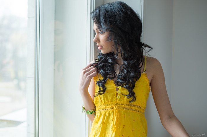 Woman with black curly hair in a yellow dress by the window