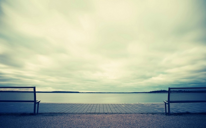 Two empty benches by a lake under cloudy sky
