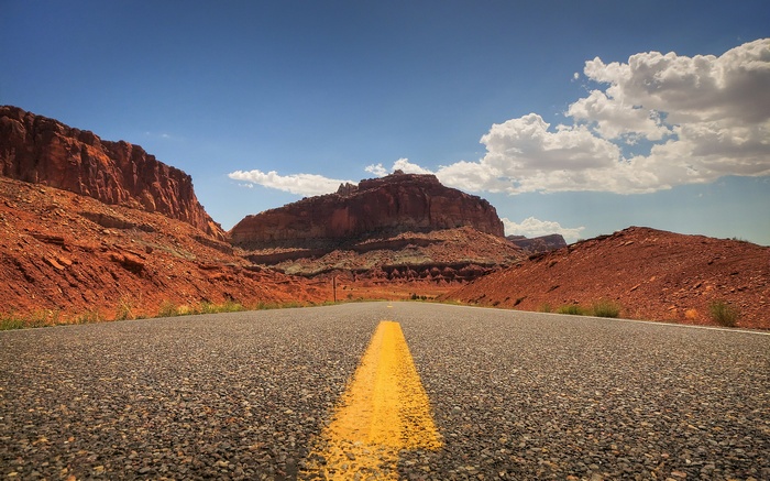 Road through red rock formations under a blue sky