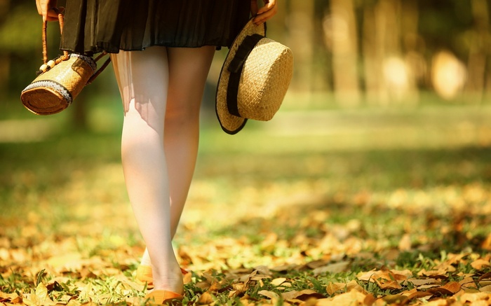 Woman in skirt holding a hat and bag outdoors
