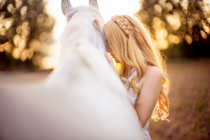 Woman with blonde hair and a white horse at sunset