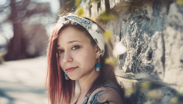 Woman with red hair and bandana leaning on a stone wall