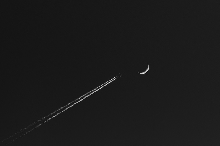 Airplane leaving contrails near a crescent moon