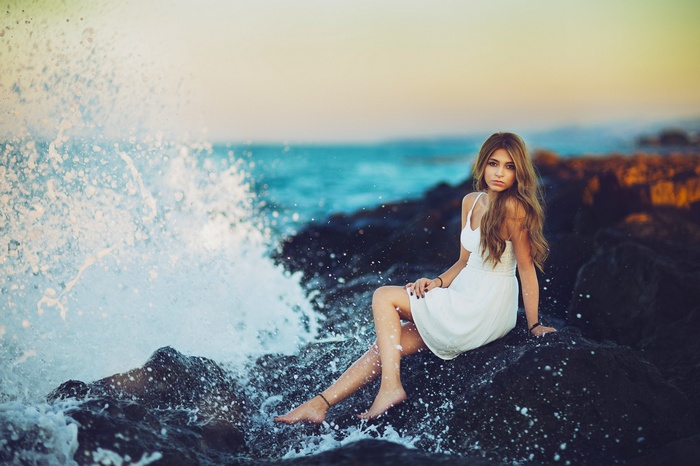 Woman in white dress sitting on rocks by the sea
