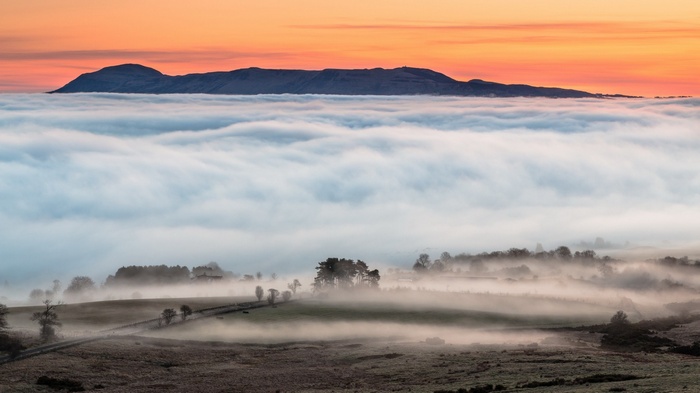 Mountain range above clouds at sunset with mist in valley
