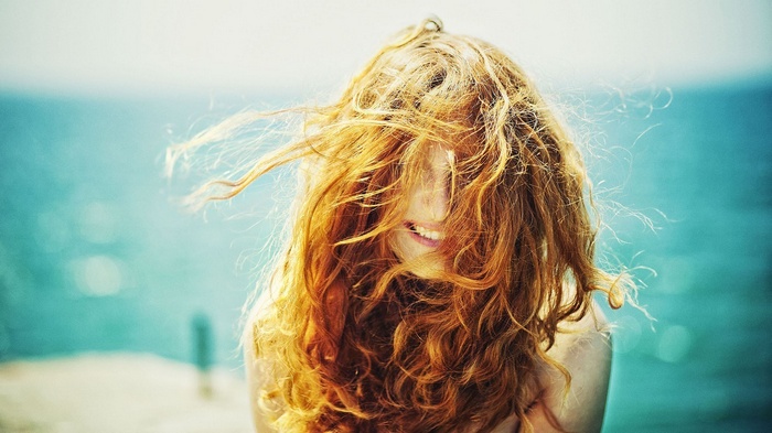 Redhead woman with hair blowing in the wind by the sea