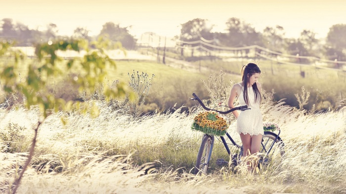 Woman in white dress with a bicycle in a field
