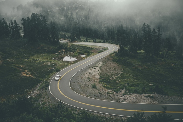 Winding mountain road through a foggy forest with a car