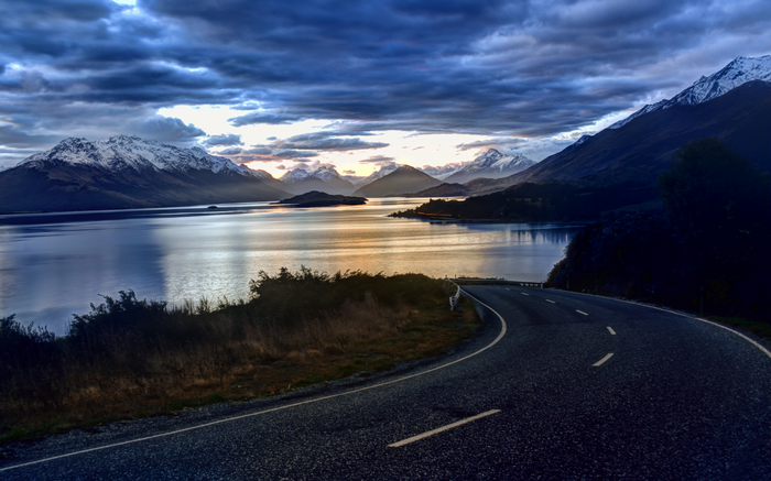 Road winding along a lake with snow-capped mountains