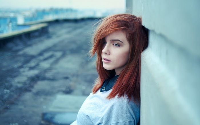 Redhead woman leaning against a wall on a rooftop