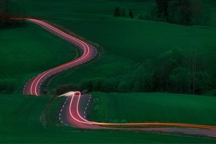 Long exposure of a winding road with light trails in a green landscape