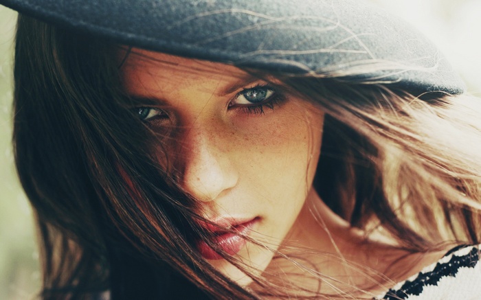 Woman with hat and hair in face, looking at viewer
