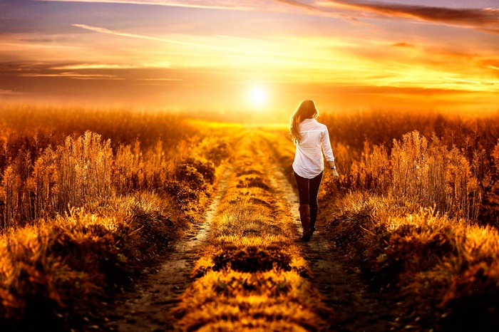 Woman walking on a dirt path at sunset