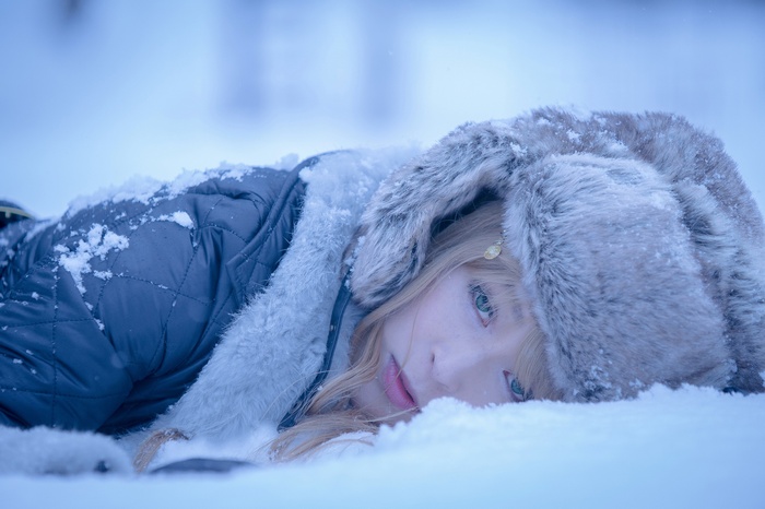 Woman in fur hat lying in the snow