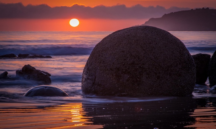 Sunset over the sea with large boulders on the beach
