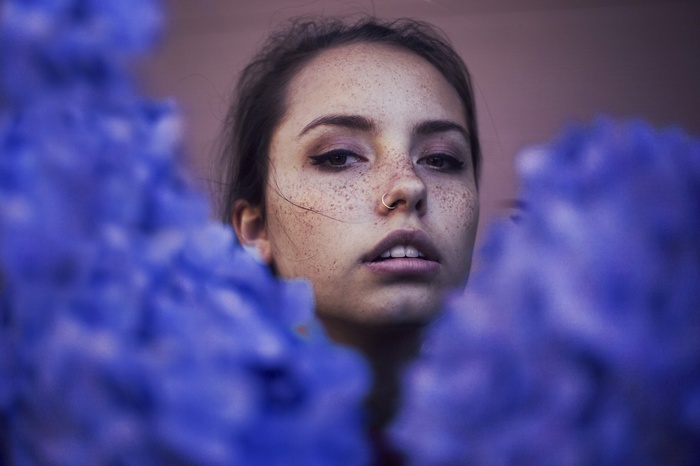 Woman with freckles and nose ring surrounded by blue smoke
