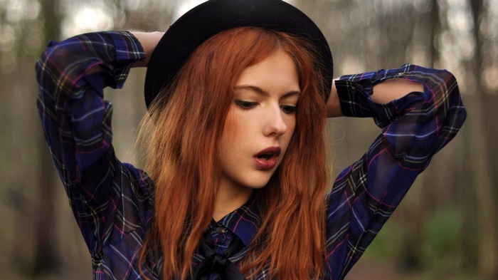 Redhead woman with arms up wearing a plaid shirt and hat