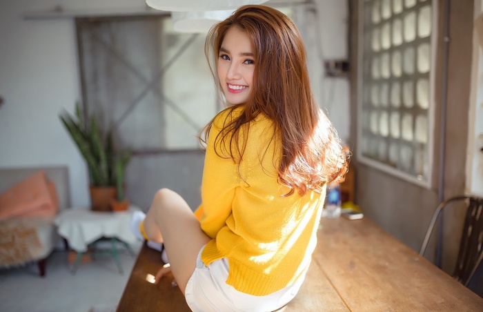 Asian woman in yellow sweater and white shorts smiling