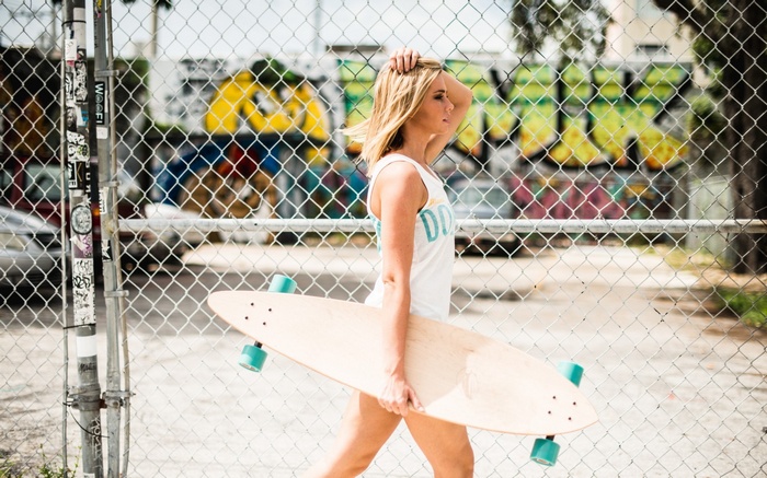 Woman holding a skateboard near a chain-link fence