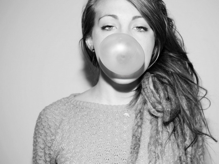 Woman blowing a bubble gum bubble with dreadlocks