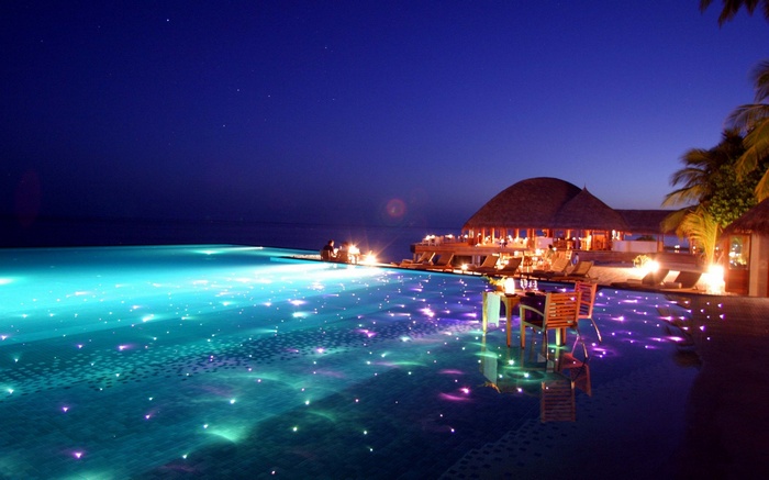 Infinity pool at night with glowing lights and a resort
