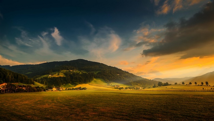 Sunset over a green valley with a forest