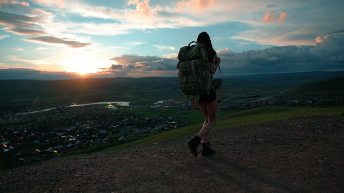Woman with backpack on a hill at sunset