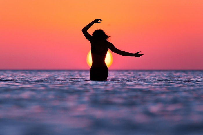 Silhouette of a woman dancing in the ocean at sunset