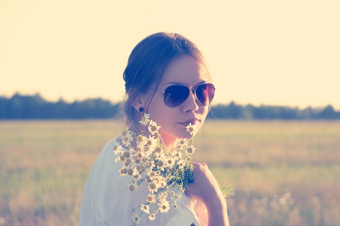 Woman in sunglasses holding daisies in a field