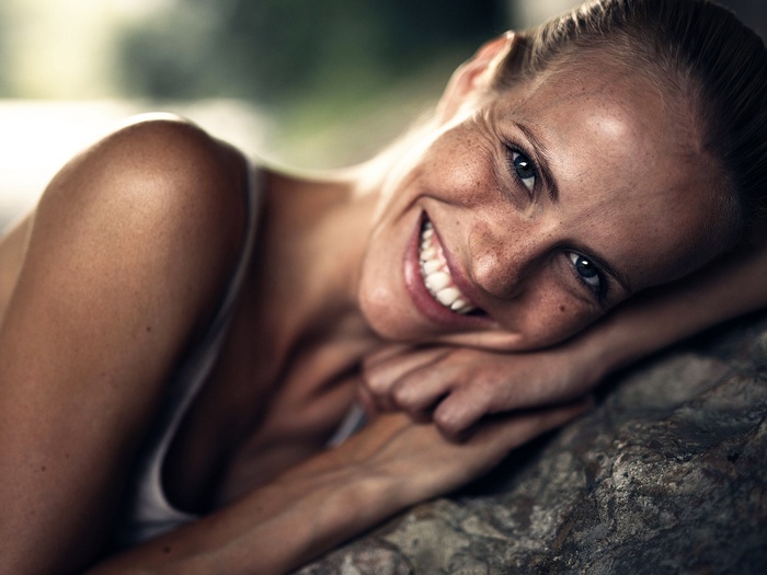 Woman with freckles smiling, resting on a rock