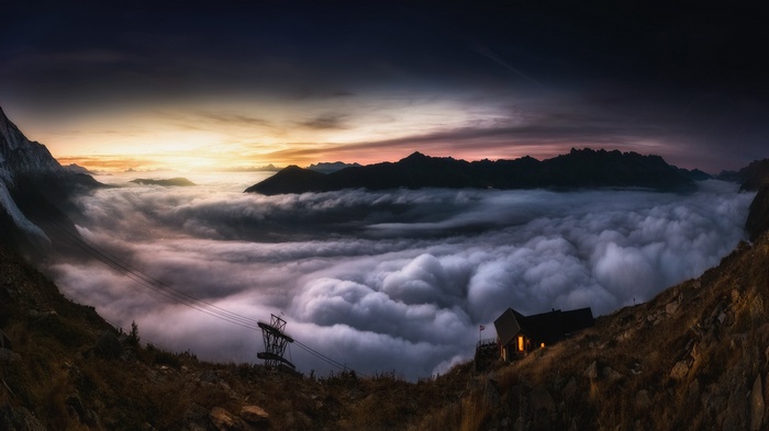 Mountain cabin above clouds at sunset with cable car