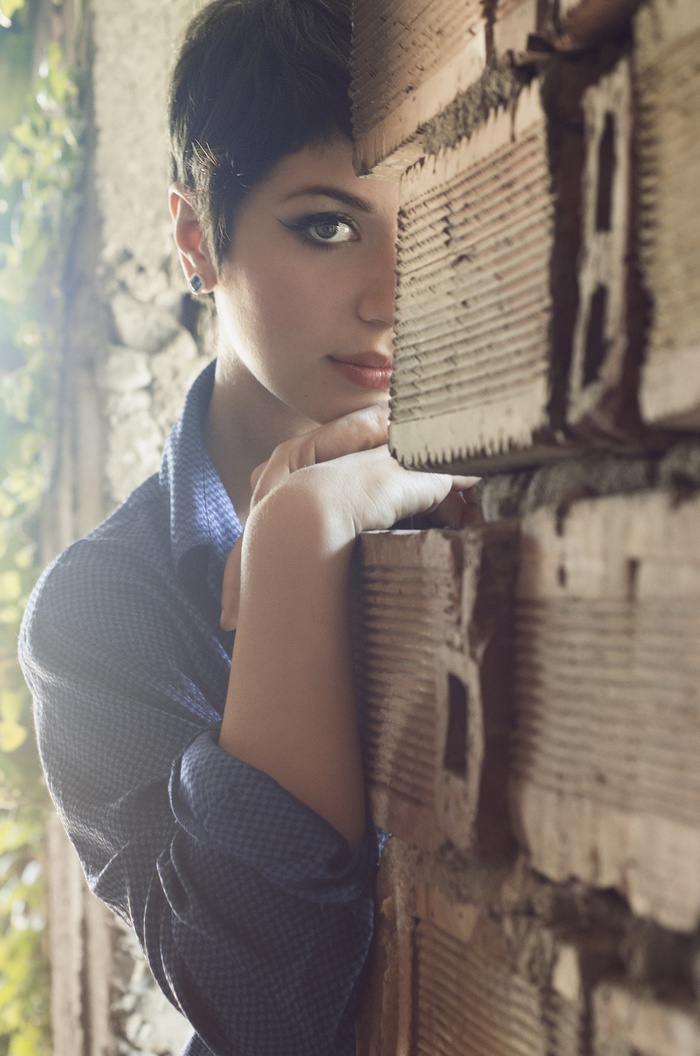 Woman with short hair leaning on a brick wall
