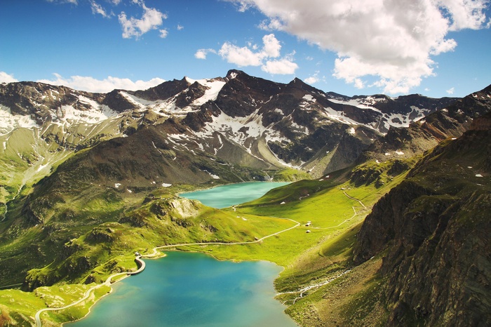Two turquoise mountain lakes surrounded by green hills and snow-capped peaks