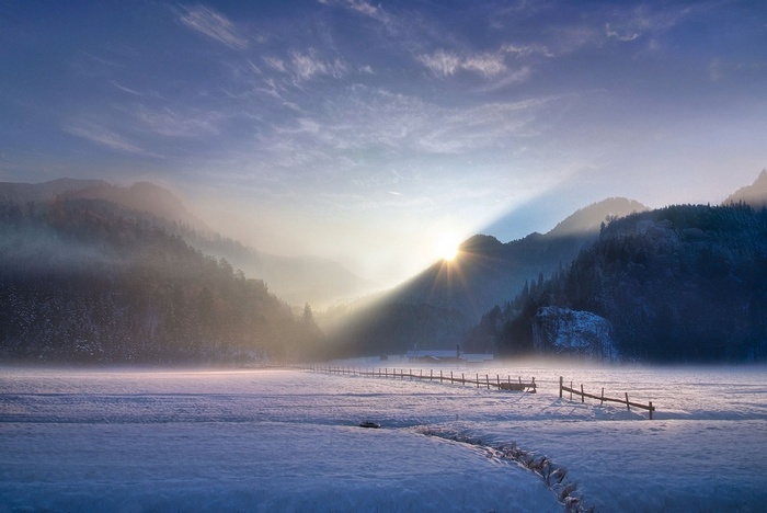 Winter sunset over snowy mountains with sun rays and mist