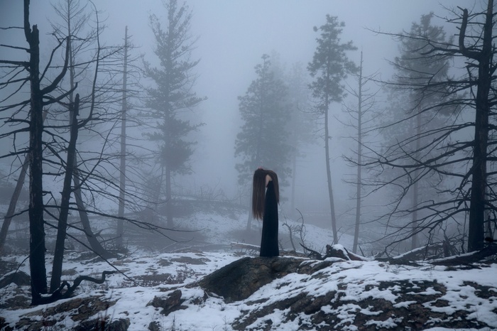 Woman in a dark dress in a foggy winter forest