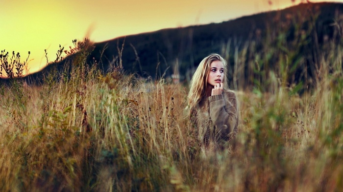 Woman in a sweater in a field at sunset