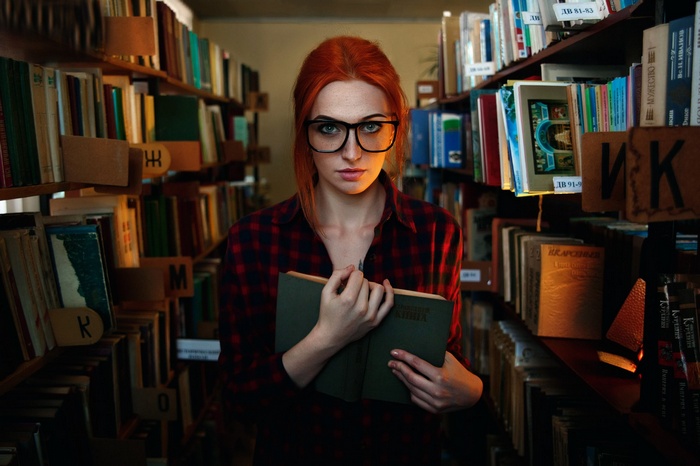Woman with glasses holding a book in a library