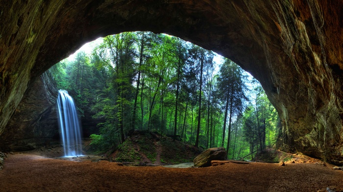 Waterfall cascading from a cave into a forest