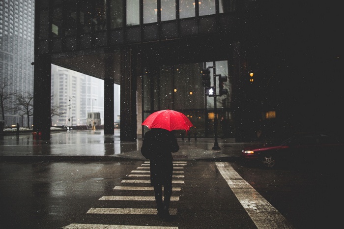 Person with red umbrella crossing street in rain