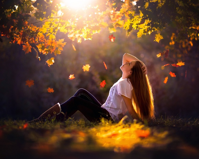 Woman sitting in autumn leaves with sunlight