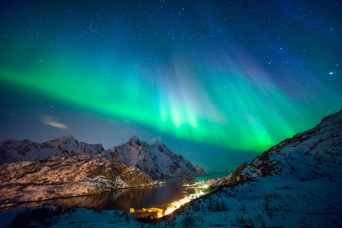 Aurora Borealis over snowy mountains and a village