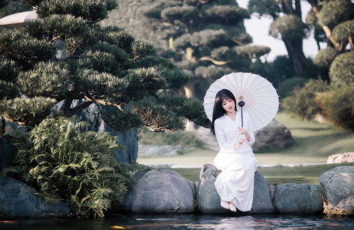 Asian woman in white dress holding umbrella in garden