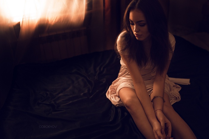 Woman in a dress sitting on a bed by the window