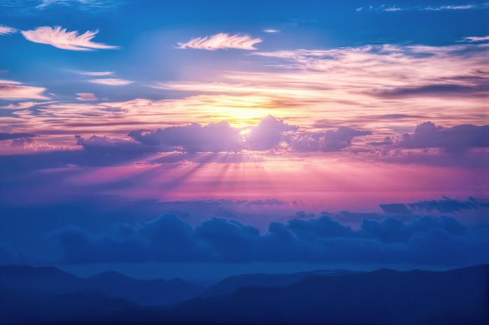 Sunlight beams through colorful clouds over mountains