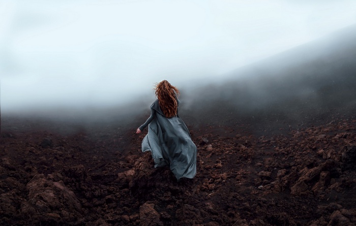 Woman with long red hair in a grey dress in the mist