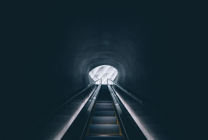 Escalator leading to a bright opening in a dark tunnel