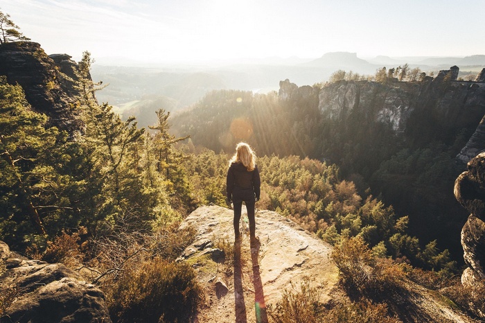 Woman standing on a cliff overlooking a forest landscape