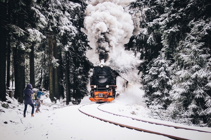 Steam train in a snowy forest with people