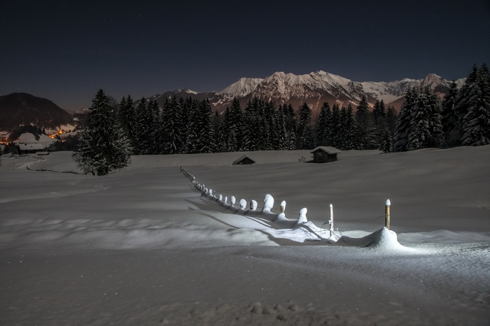 Snowy mountain landscape at night with a fence