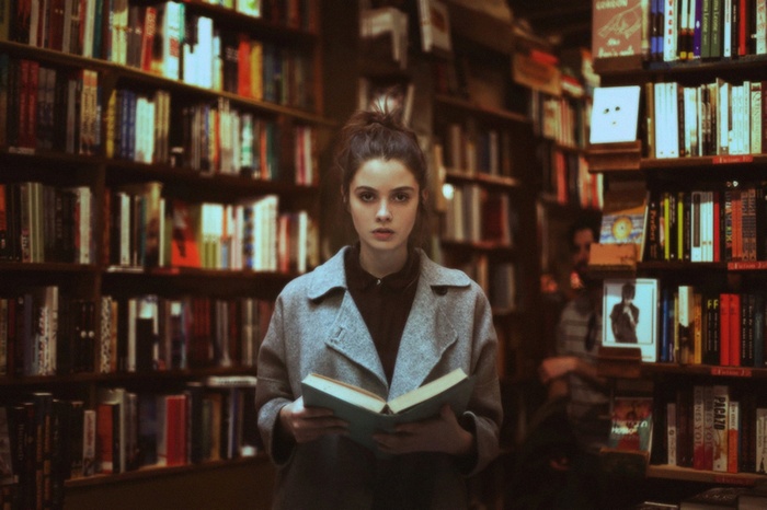 Woman in grey coat reading a book in a library